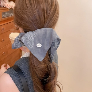 Detail of grey paisley bow hair tie with white decorative button on brown curly hair