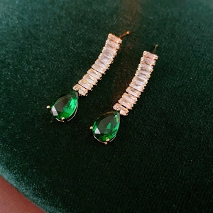 Macro shot of gold teardrop earrings with green stones on dark green velvet background