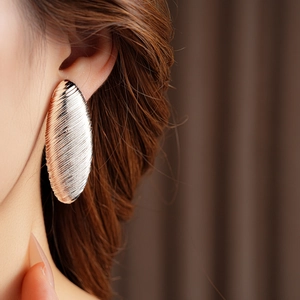 Close-up of rose gold oval earring with striped texture worn by a model