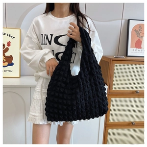 Close-up of black tote bag with bubble pleat texture held by a model in a stylish setting