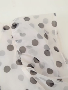 Detailed close-up of white organza fabric with black polka dots and ruffle edge