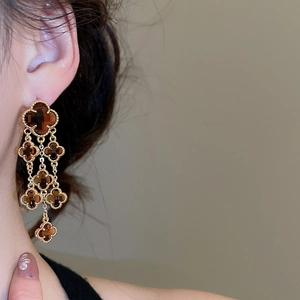 Detail view of crystal flower tassel earrings with amber clover pendants on a model