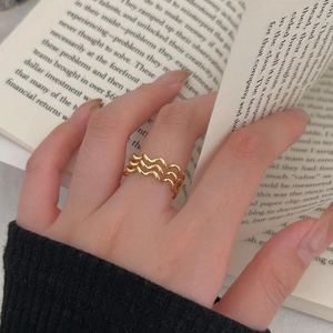 Detail of a minimalist gold wavy layered ring worn by a model over an open book