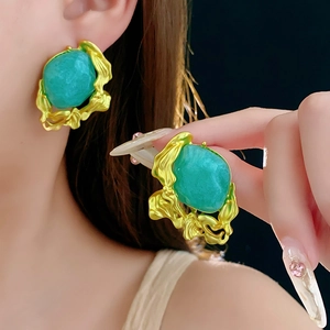 Detailed view of vintage emerald green earrings with fluid gold metal frames on model