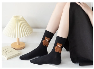 Detailed close-up of a black crew sock featuring a 3D plush brown teddy bear patch