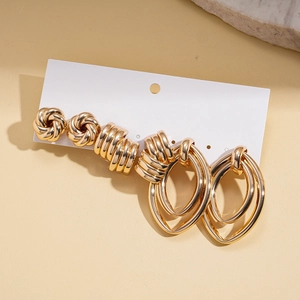 Close-up of three pairs of gold metal earrings with knot and spiral designs on a white card
