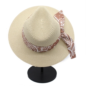 Top view of beige straw sun hat featuring a paisley ribbon bow on a white background