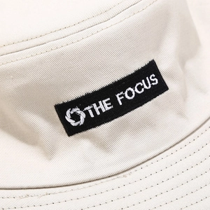 Macro detail of THE FOCUS embroidery and woven label on a beige cotton bucket hat