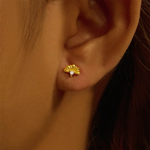 Close-up of gold fan-shaped cartilage stud earring with clear gemstone on ear
