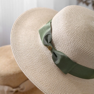 Macro detail of beige woven straw sun hat with an olive green ribbon and metal emblem