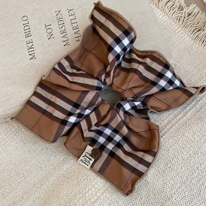 Detailed close-up of a plaid hair scrunchie with a brown floral button and fabric label