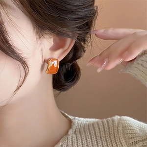 Close-up of caramel orange enamel square stud earring with gold border on model