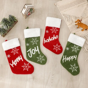Plush Christmas stockings in red and green with festive embroidery on wooden background