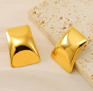Détail macro de boucles d'oreilles carrées concaves dorées sur un support en pierre