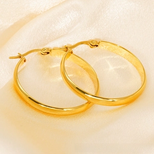 Close-up of polished gold hoop earrings featuring secure clasp on beige silk fabric