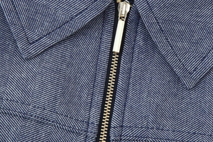 Detail der blauen Fischgrät-Stofftextur mit goldenem Metallreißverschluss und Nähten