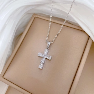 Macro shot of a silver titanium steel cross necklace with sparkling crystal inlay on silk