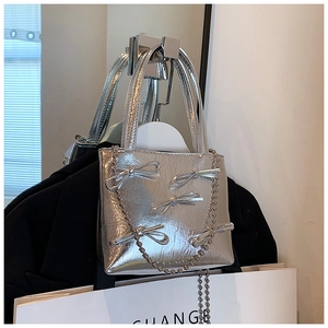 Silver metallic handbag with bow details and bead chain strap shown in a lifestyle setting