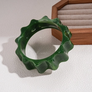 Detail of dark green acrylic bangle with marbled pattern and wavy geometric edges