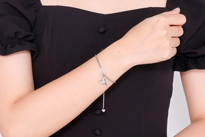 Close-up of a silver heart charm bracelet with adjustable chain worn by a female model