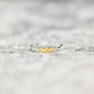 Minimalist s925 silver infinity ring with a polished golden accent on a stone surface