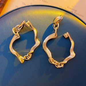 Close-up of golden irregular twisted metal earrings on a dark display stand