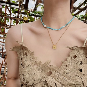 Layered gold necklace with square V pendant and turquoise bead chain on female neck
