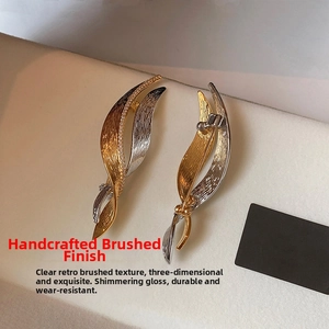 Detail of leaf-shaped brooch showing hand-brushed gold and silver textures with zircons