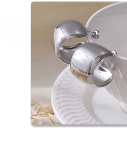 Close-up of wide polished silver C-shape earrings hanging on a white ceramic cup edge