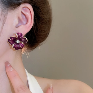 Gros plan détaillé d'une boucle d'oreille fleur en émail violet avec bordure dorée
