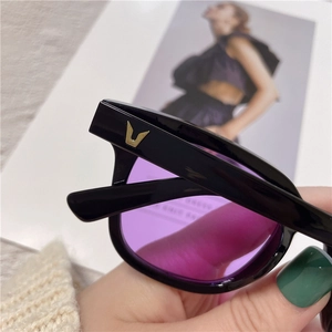 Detail shot of black sunglasses with purple lenses and golden V logo on the temple