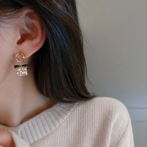 Détails de boucles d'oreilles dorées avec nœud noir et grand cristal carré sur le modèle