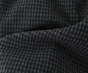 Detailed macro view of dark houndstooth wool fabric texture with soft pleated details