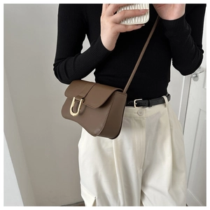 Close-up of caramel brown shoulder bag with a vintage gold horseshoe buckle on model