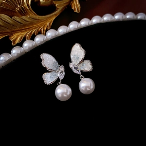 Macro detail of silver butterfly earring with cubic zirconia and round white pearl drop