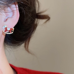 Gros plan sur les boucles d'oreilles cheval à bascule en émail rouge et doré
