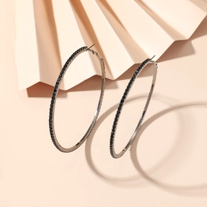 Macro detail of 8cm hoop earrings with black rhinestones on a warm textured background