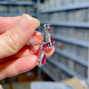Macro detail of hand-held silver drop earring with red pear-cut zircon and white stones