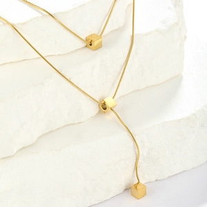 Minimalist gold snake chain necklace featuring three sleek cube pendants on white stone