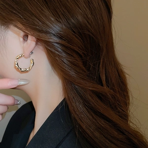 Detailed view of C-shaped golden earrings with hammer texture and sparkling diamonds