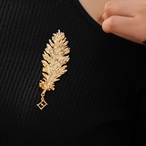 Macro detail of gold leaf feather brooch with inlaid crystals on black knit fabric