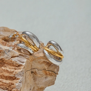 Close-up of C-shaped mixed gold and silver spiral twist earrings on natural rock base