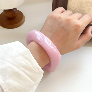 Close-up of minimalist chunky pink resin bangle on wrist in a warm home setting