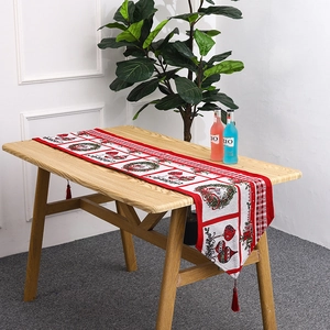 Detail of red Christmas table runner featuring holiday wreaths, gift patterns and tassels