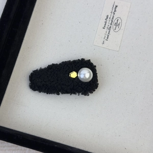 Detail of black faux lamb wool hair clip featuring a white pearl and gold metal accent