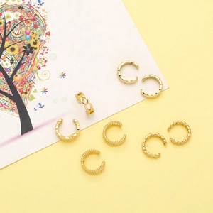Dettaglio del set di ear cuff dorati e un anello infinito su sfondo giallo acceso