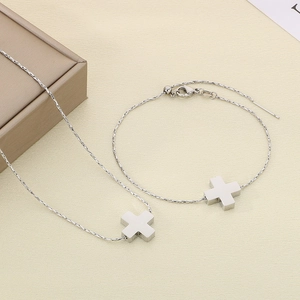 Detailed view of silver stainless steel cross pendant necklace and bracelet set on beige background