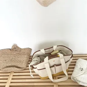 Detail of multi-pocket canvas mommy bag with contrast trim on a rustic wooden bench