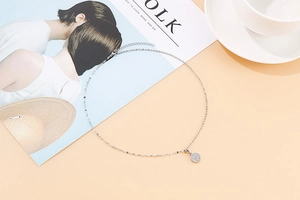 Flat lay of a silver coin pendant necklace with a white coffee cup and a magazine