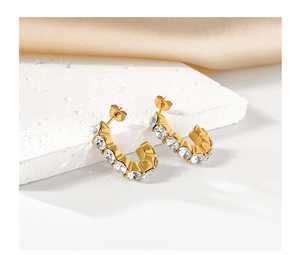 Macro detail of gold-plated C-shaped hoop earrings featuring sparkling zircon stone pavé